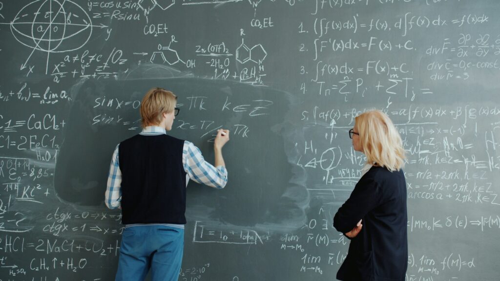 Two people working through equations on a blackboard